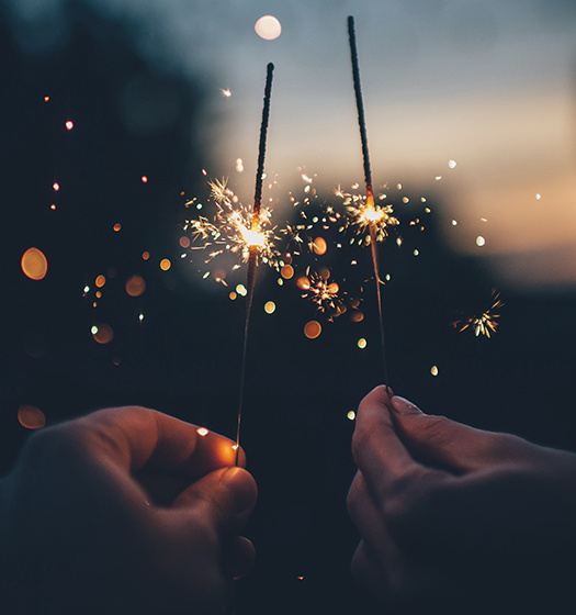 Two hands holding sparklers at dusk